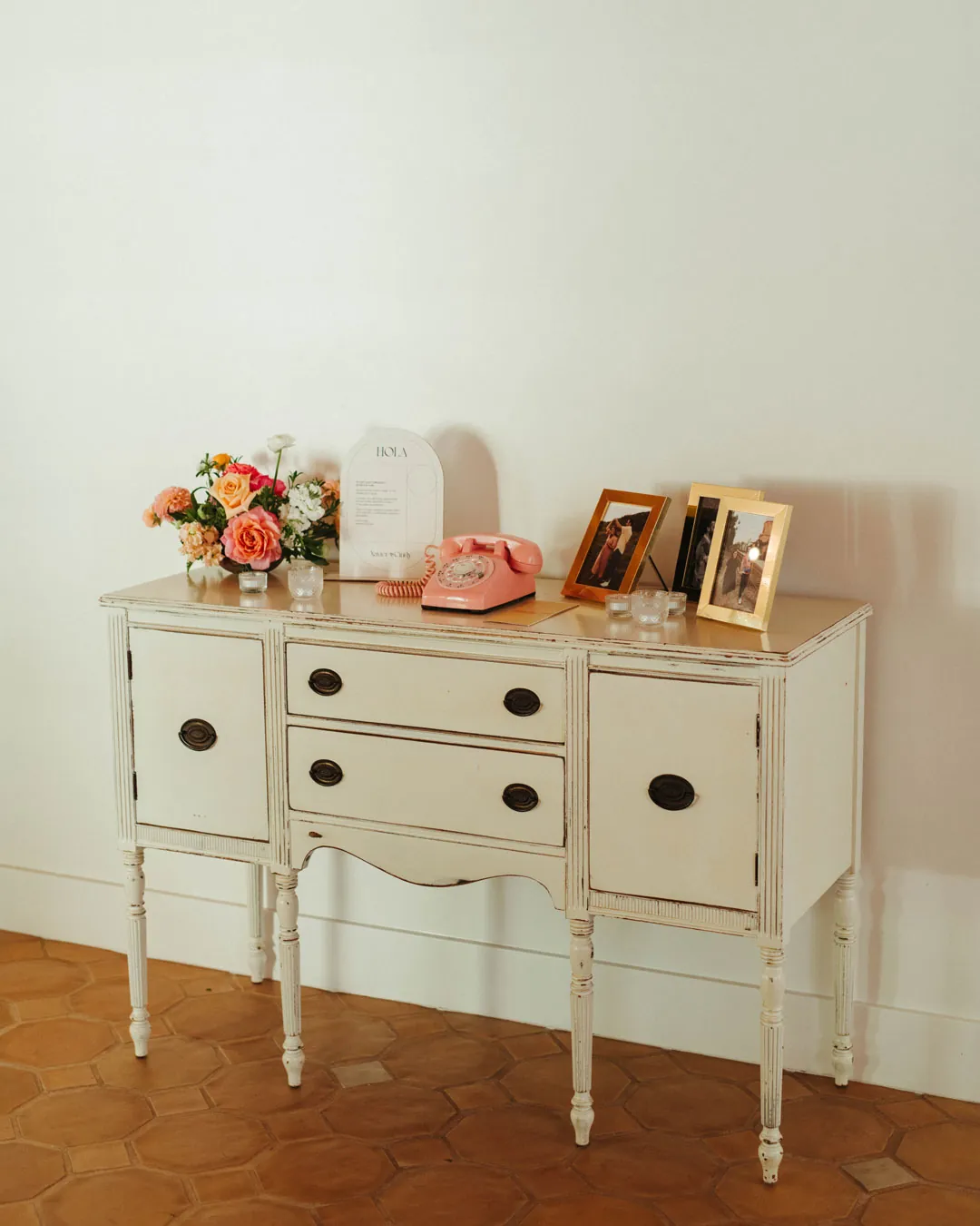 Flowers and framed photographs decorate a white console table.