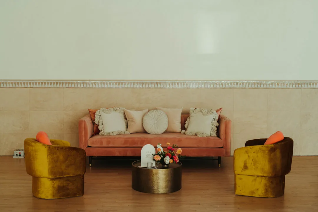A pink lounge sofa sits between two mustard-colored chairs.