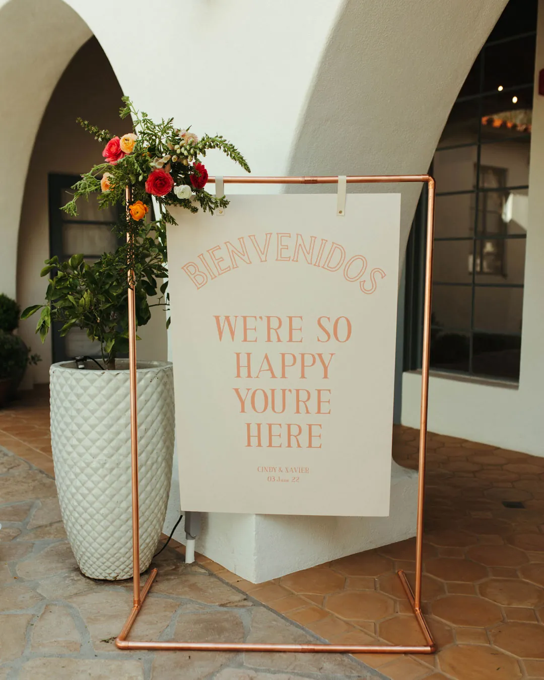 A wedding welcome sign stands beside a courtyard arch.