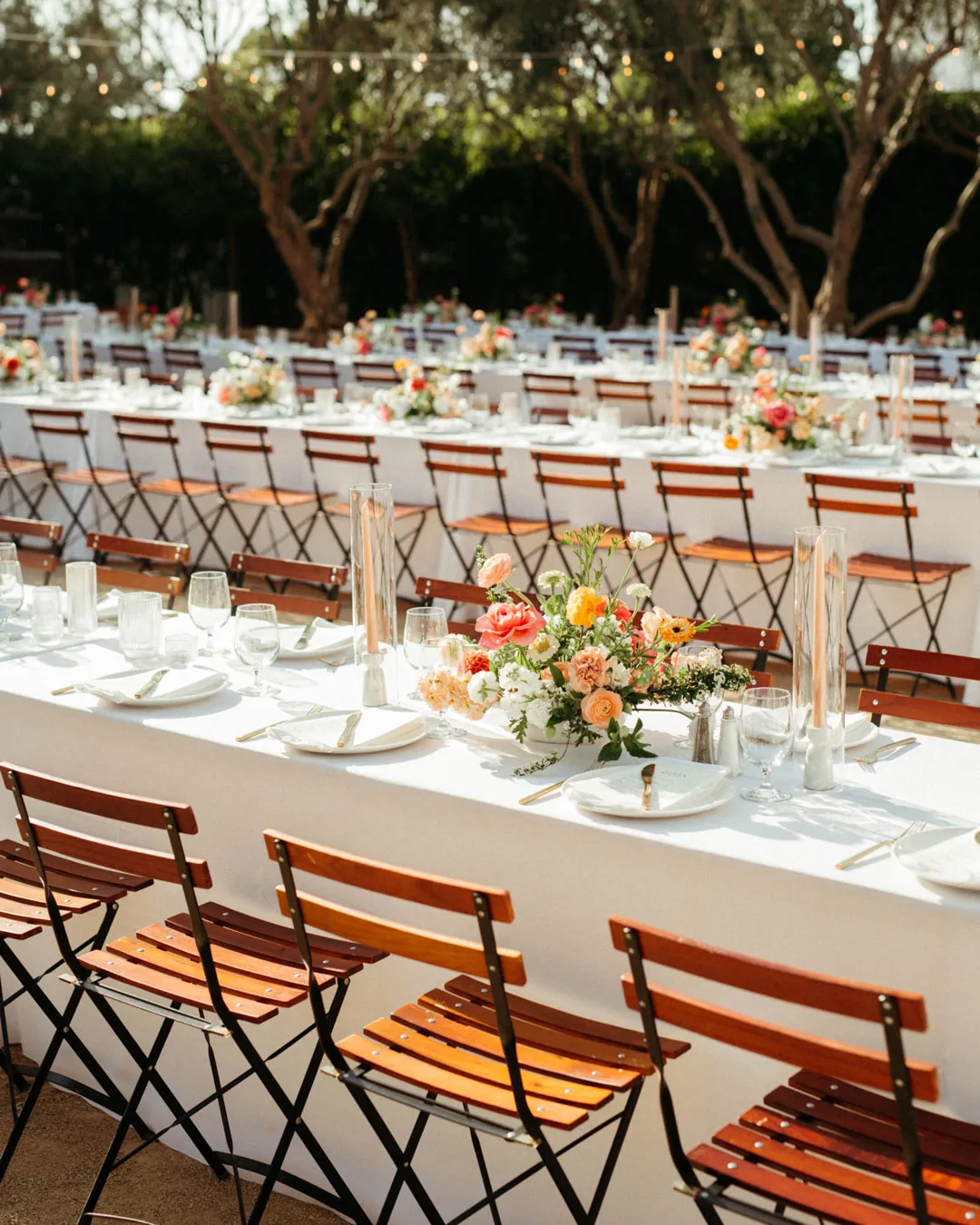 Long courtyard tables have white linens and colorful flowers.