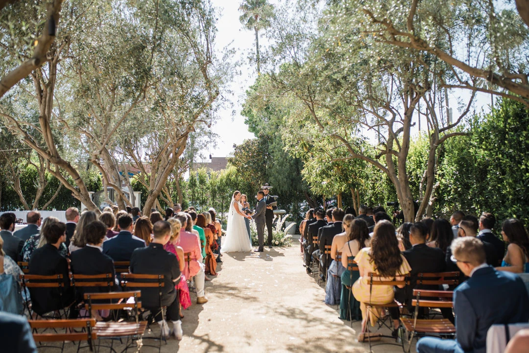 Guests watching an outdoor ceremony from rows of wooden chairs.