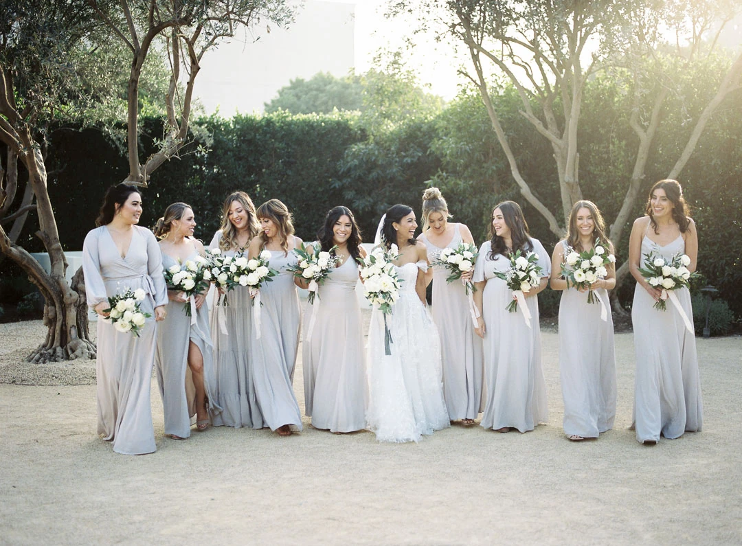 Bride posing with bridesmaids beneath olive trees.