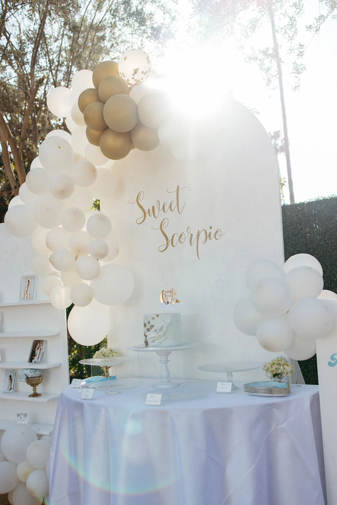 White and gold balloons frame an outdoor dessert display.