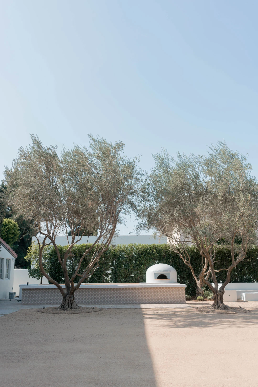 Wide courtyard with olive trees and a pizza oven.