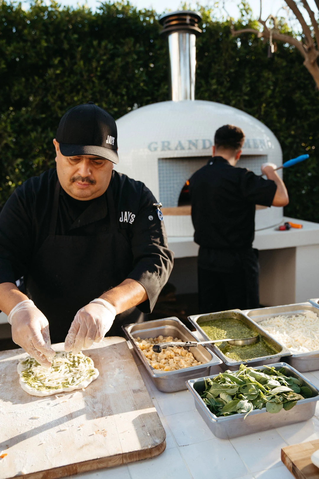 Staff member adds toppings to pizza dough.