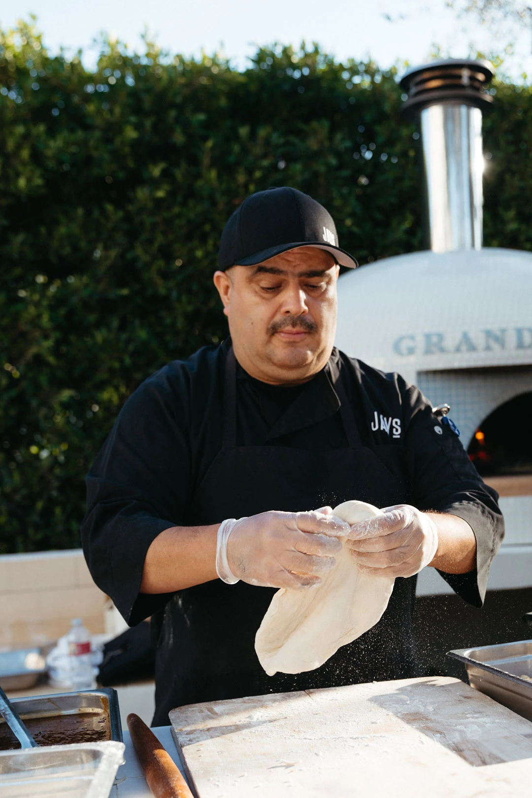 Staff member stretches pizza dough at an outdoor station.