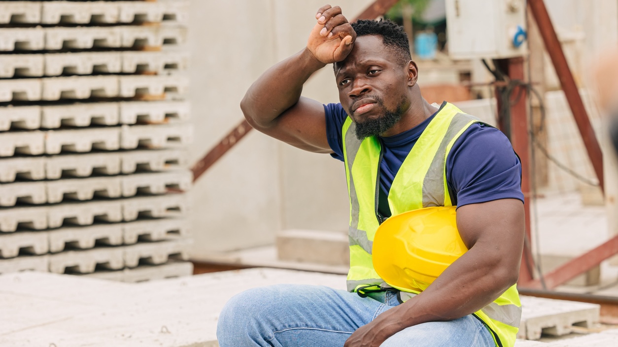 A construction worker wipes sweat from his brow.
