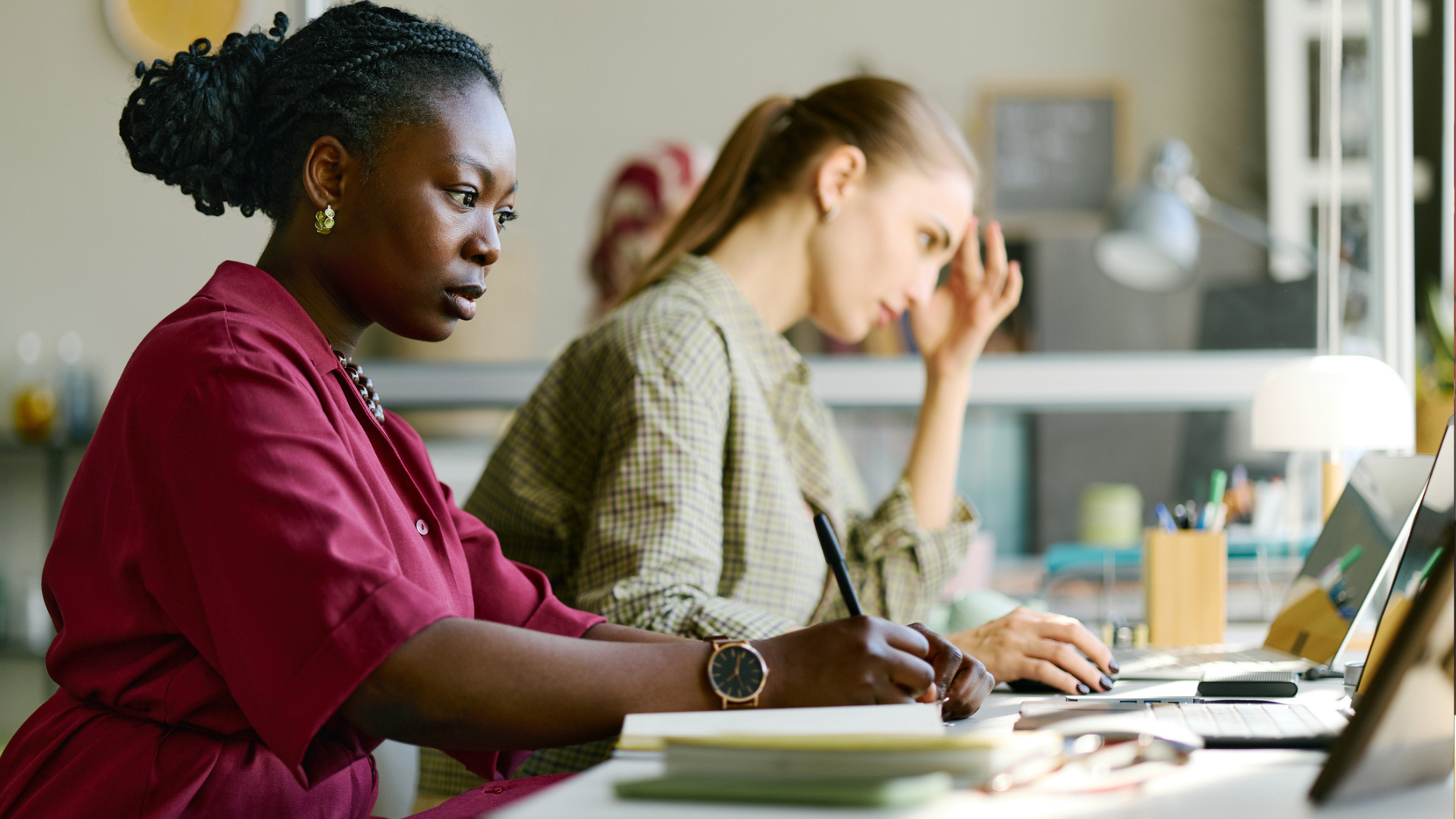 Two women sit at a desk and work. 