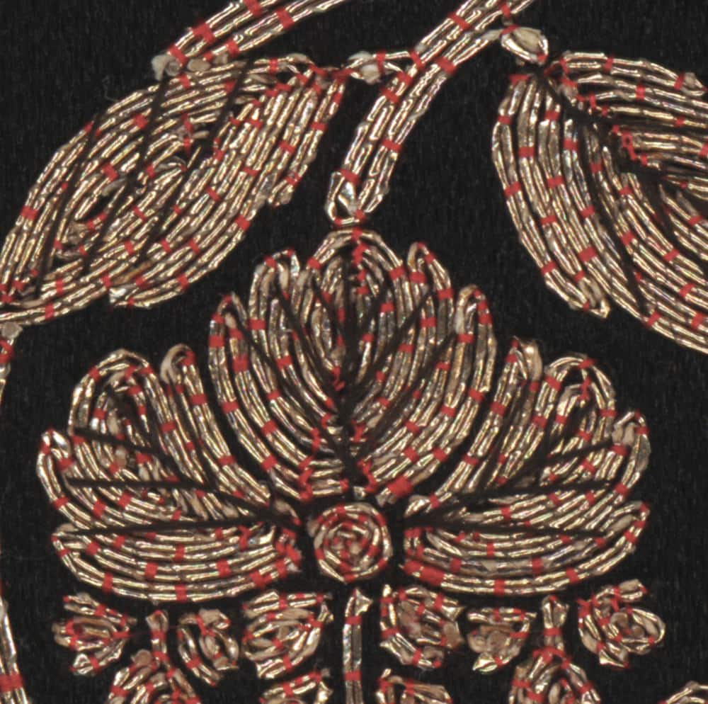 Intricate gold and red embroidery of a floral design on black fabric