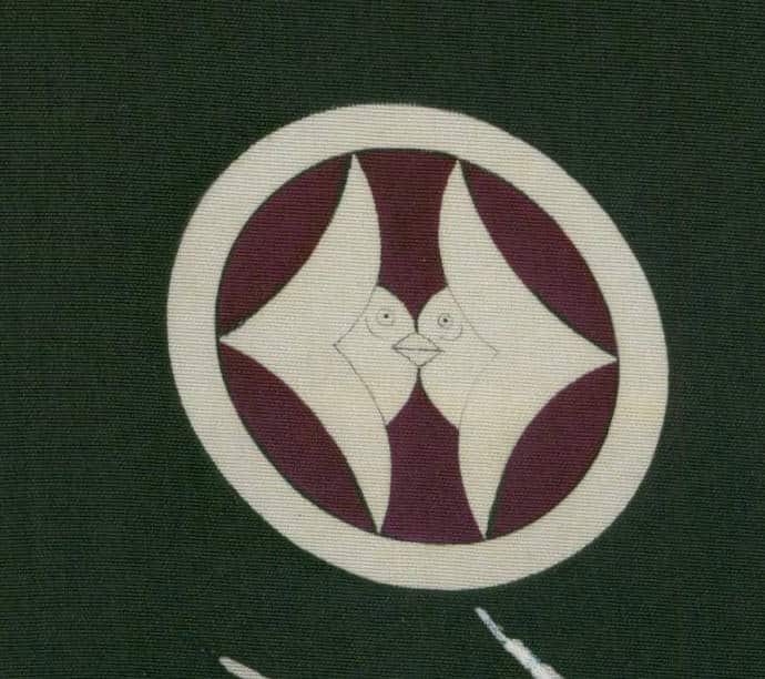 Geometric circular emblem with stylized bird-like faces in maroon and white