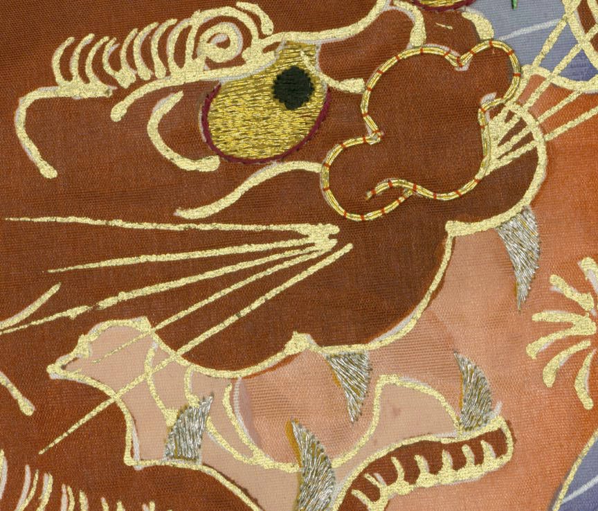 Embroidered golden abstract creature on brown textile with swirling lines