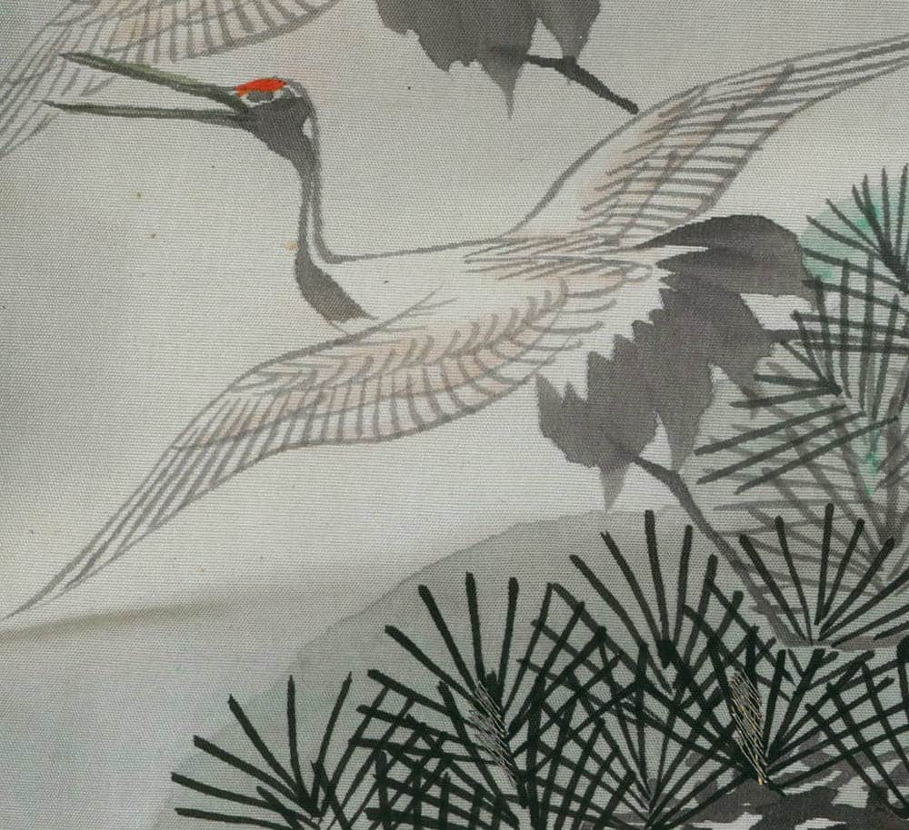 Japanese crane with red crown flying near pine branches