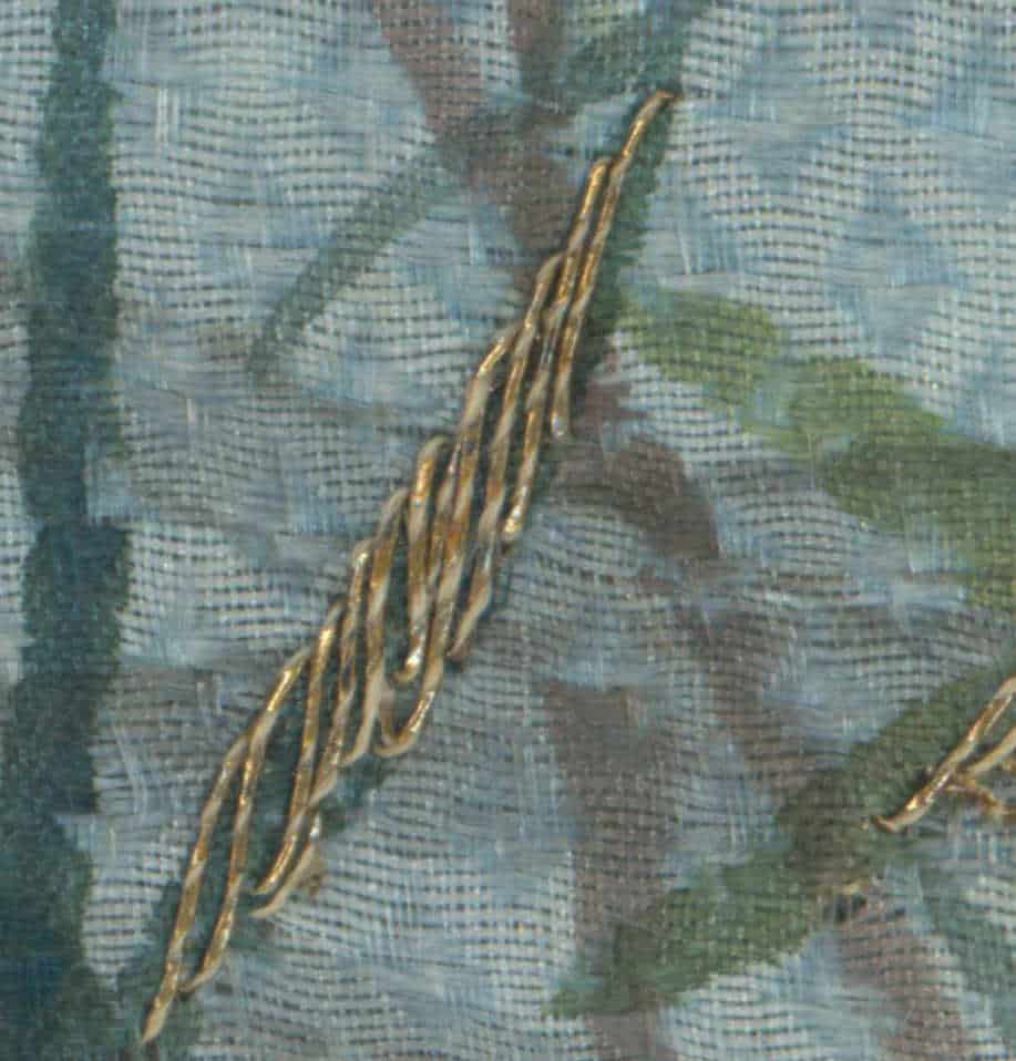 Gold metallic thread or cord twisted on blue-green textured fabric background
