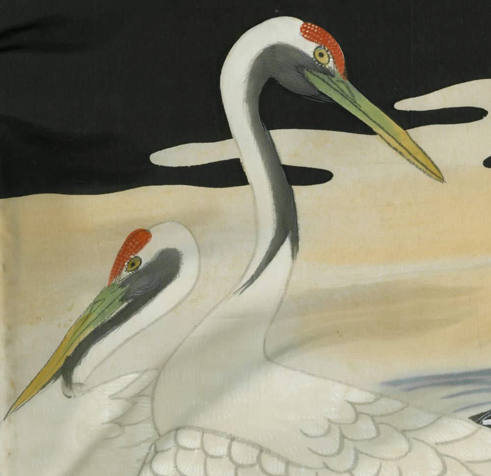 Two white cranes with red-capped heads and yellow-green beaks