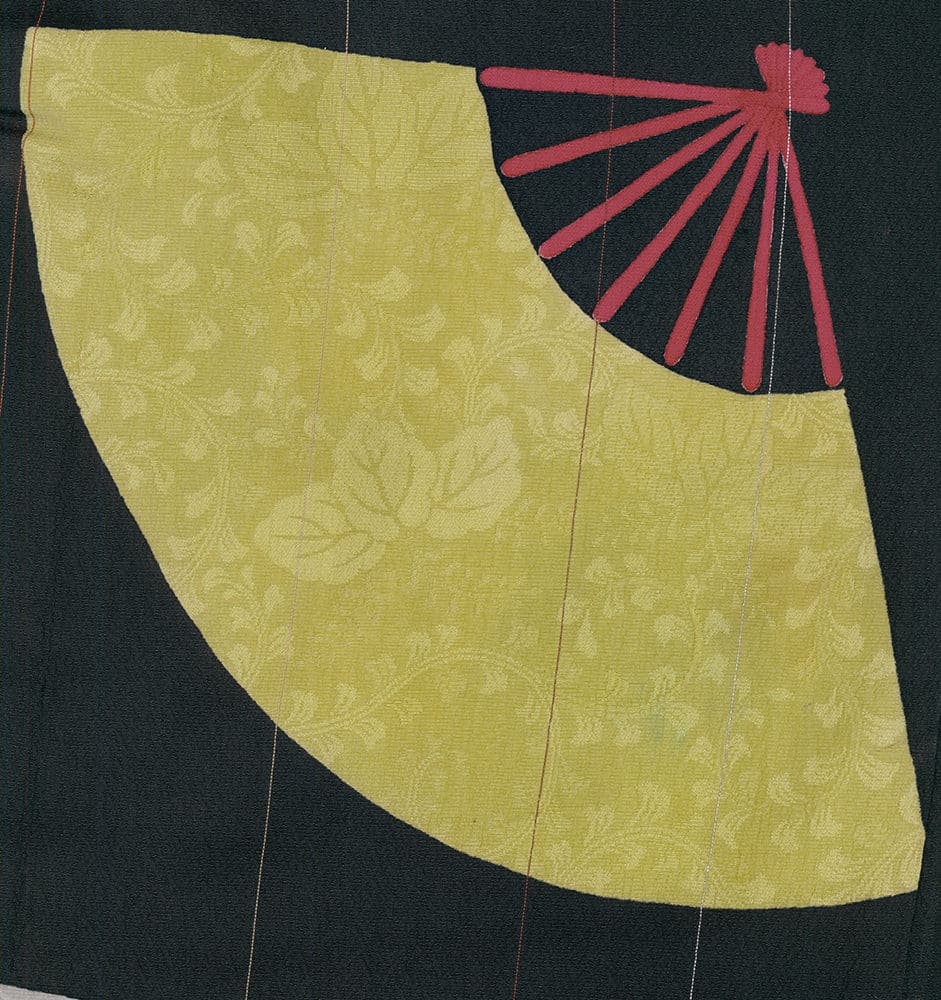 Pale yellow folded fan with red handle on dark background