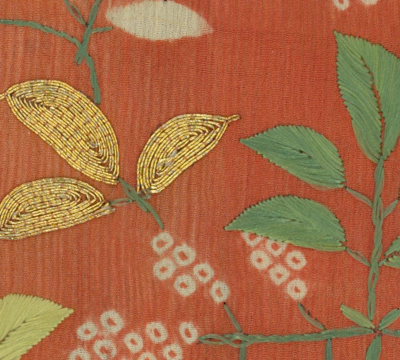 Vintage textile with golden embroidered leaves on orange background