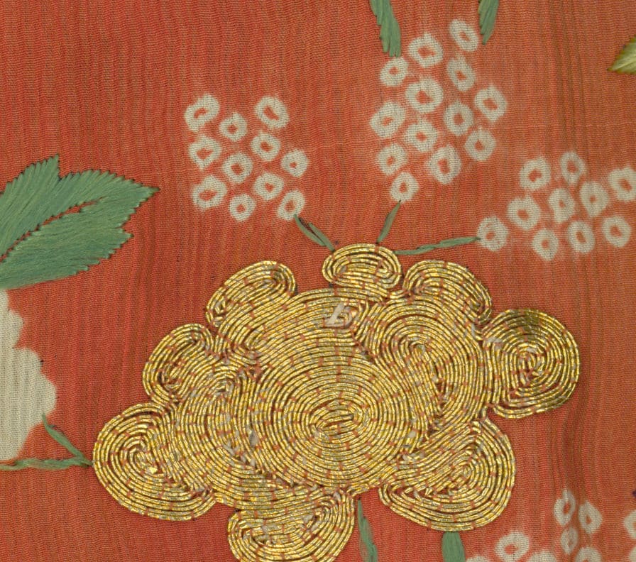 Golden embroidered flower on textured orange fabric with green leaves