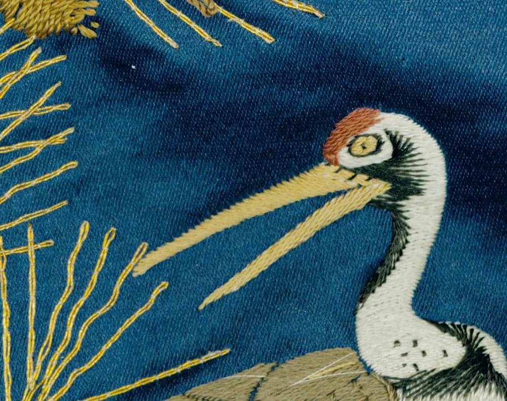 Embroidered white heron with yellow details on deep blue fabric background