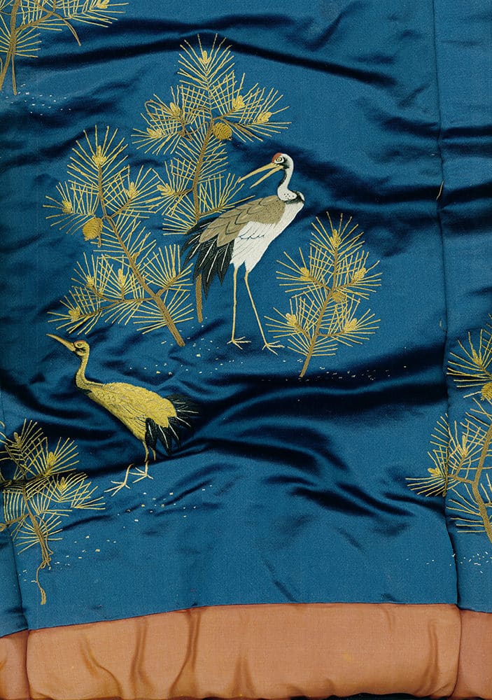 Embroidered cranes among golden pine branches on deep blue fabric