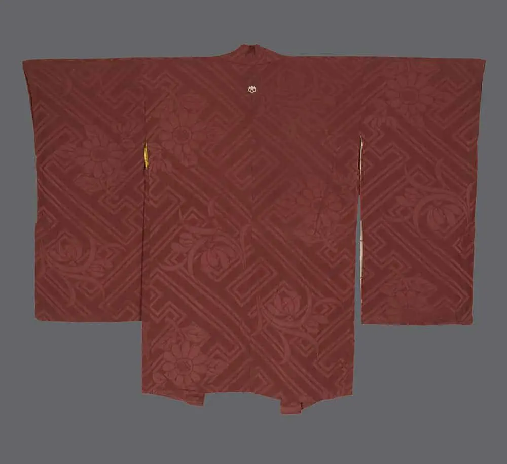 Russet-red rinzu silk haori featuring a woven chrysanthemum and key fret pattern with a white family crest.
