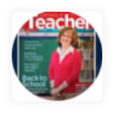 Teacher in a red sweater standing in a classroom with a chalkboard and bookshelves.