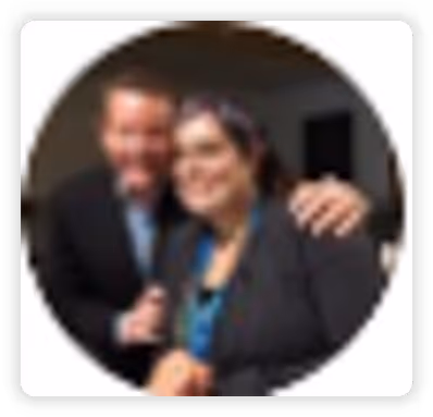 Two people smiling and posing closely together, one with arm around the other's shoulder.