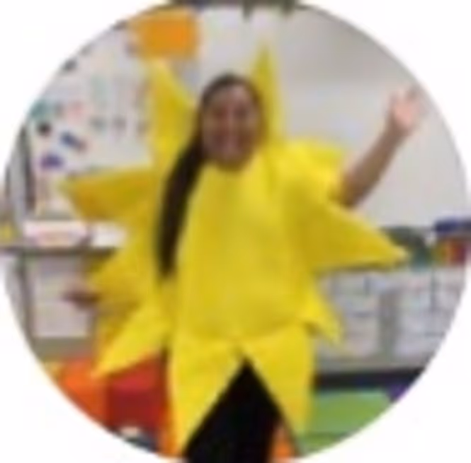 Person wearing a bright yellow sun costume with arms raised in a classroom setting.