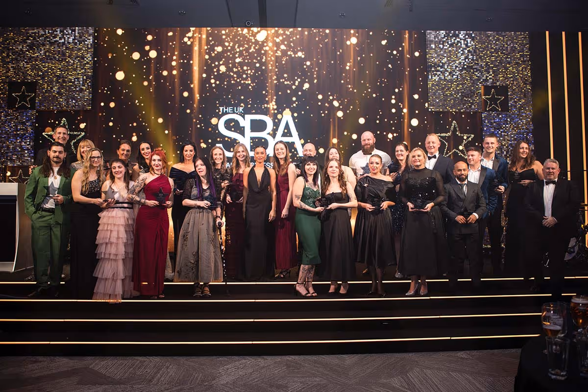 Wide-angle professional group photography from The UK Small Business Awards at The Eastside Rooms in Birmingham, featuring the full lineup of category winners holding their trophies on stage under dramatic event lighting.