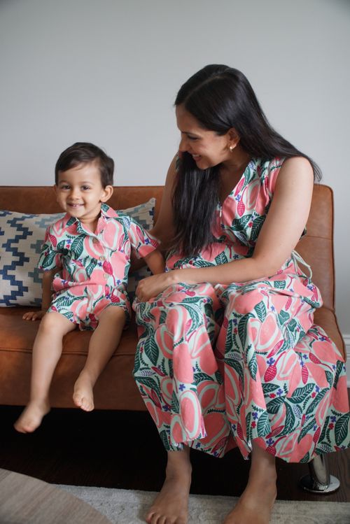 A woman and a young boy sitting on a brown leather couch, both wearing matching pink floral patterned outfits, the woman smiling at the boy who is looking towards the camera.