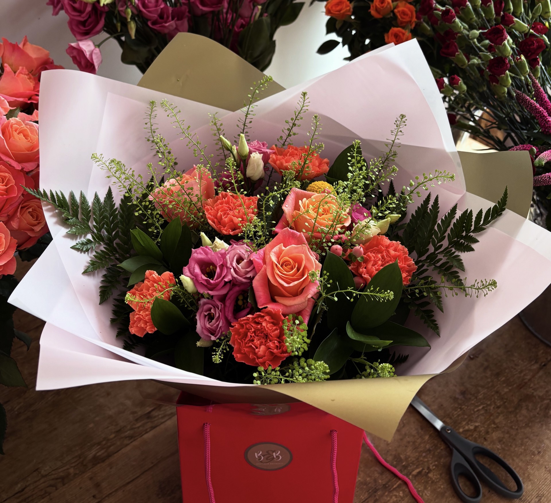 Miss piggy roses, carnations, green bell, lisianthus, craspedia and hypericum along with mixed foliages make up this beautiful, bright bouquet.