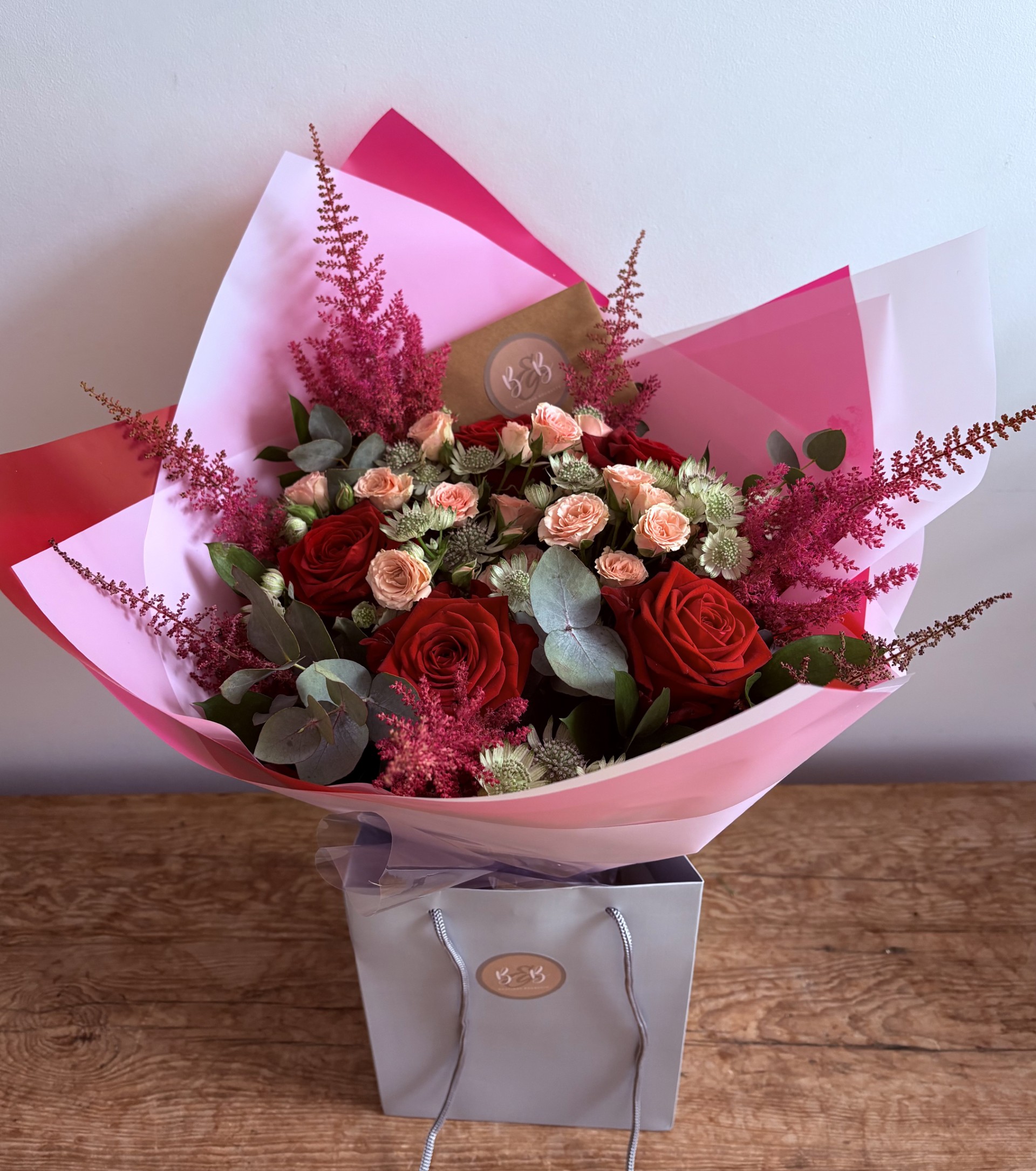 This beautiful bunch contains red roses, pink spray roses, astrantia, astilbe and foliages.