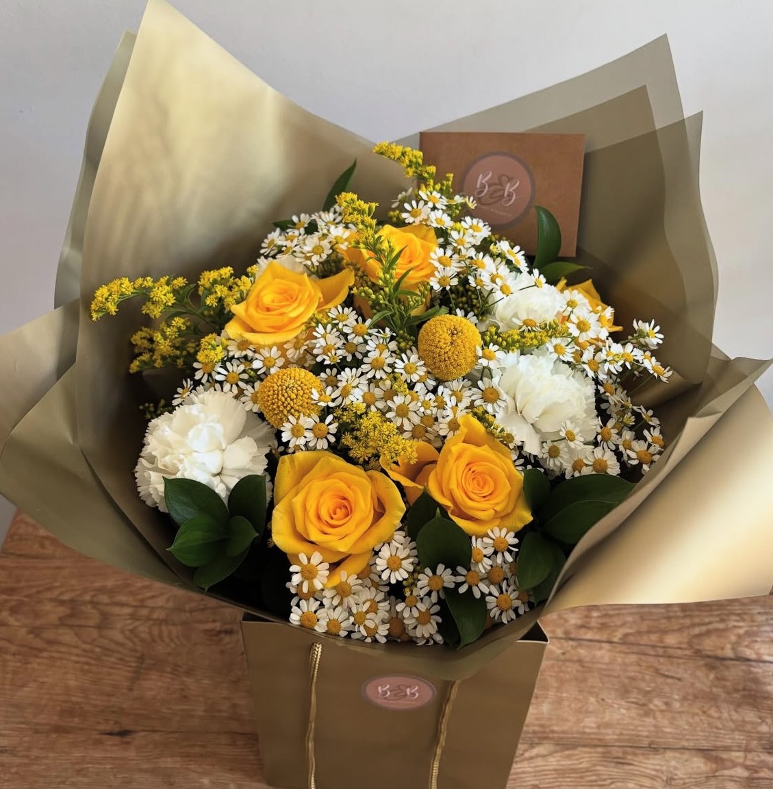 This pretty bouquet comprises a collection of warm golden roses, solidago, craspedia, tanacetum, carnations and foliages.