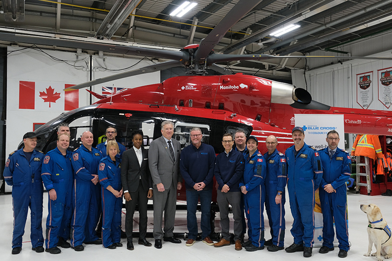 A group of STARS employees, Manitoba Blue Cross leaders and Minister of Health, Seniors and Long Term Care Uzoma Asagwara pose in front of a STARS helicopter.