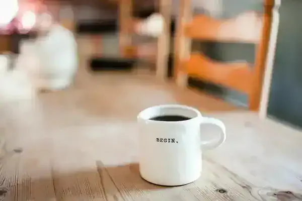 coffee mug on a table in the sunshine with the word "begin" on it