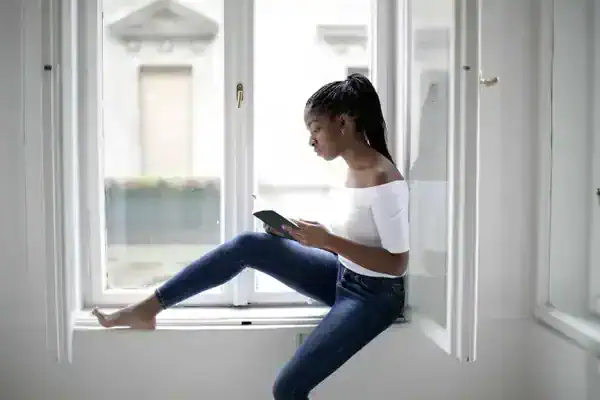young woman in a window ledge sitting and journaling