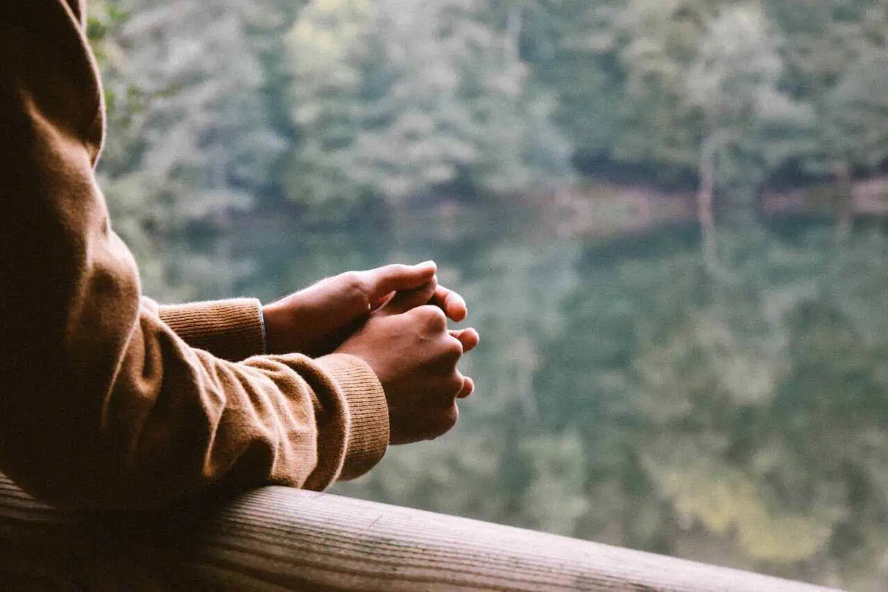 persons hands on a balcony rail overlooking greenery implying contemplation