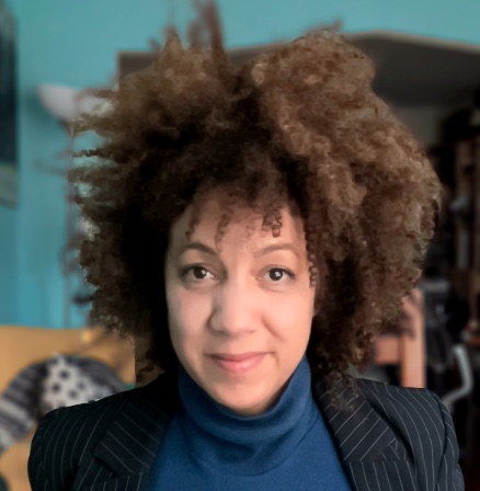 A photograph of Anna Jane McIntyre, who is looking directly at the viewer. She has brown afro hair and is wearing a blue polo neck top with a dark blue pin-striped jacket