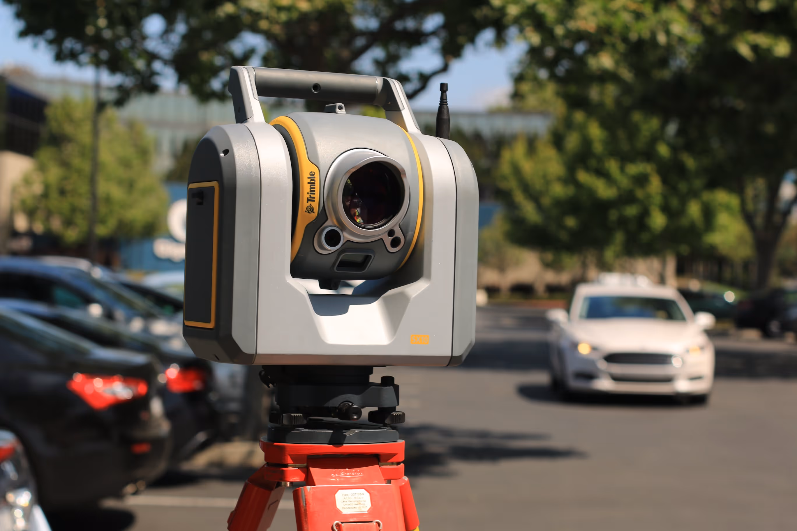 Trimble technology scanner device accurately scanning terrain outdoors near vehicle parking areas.