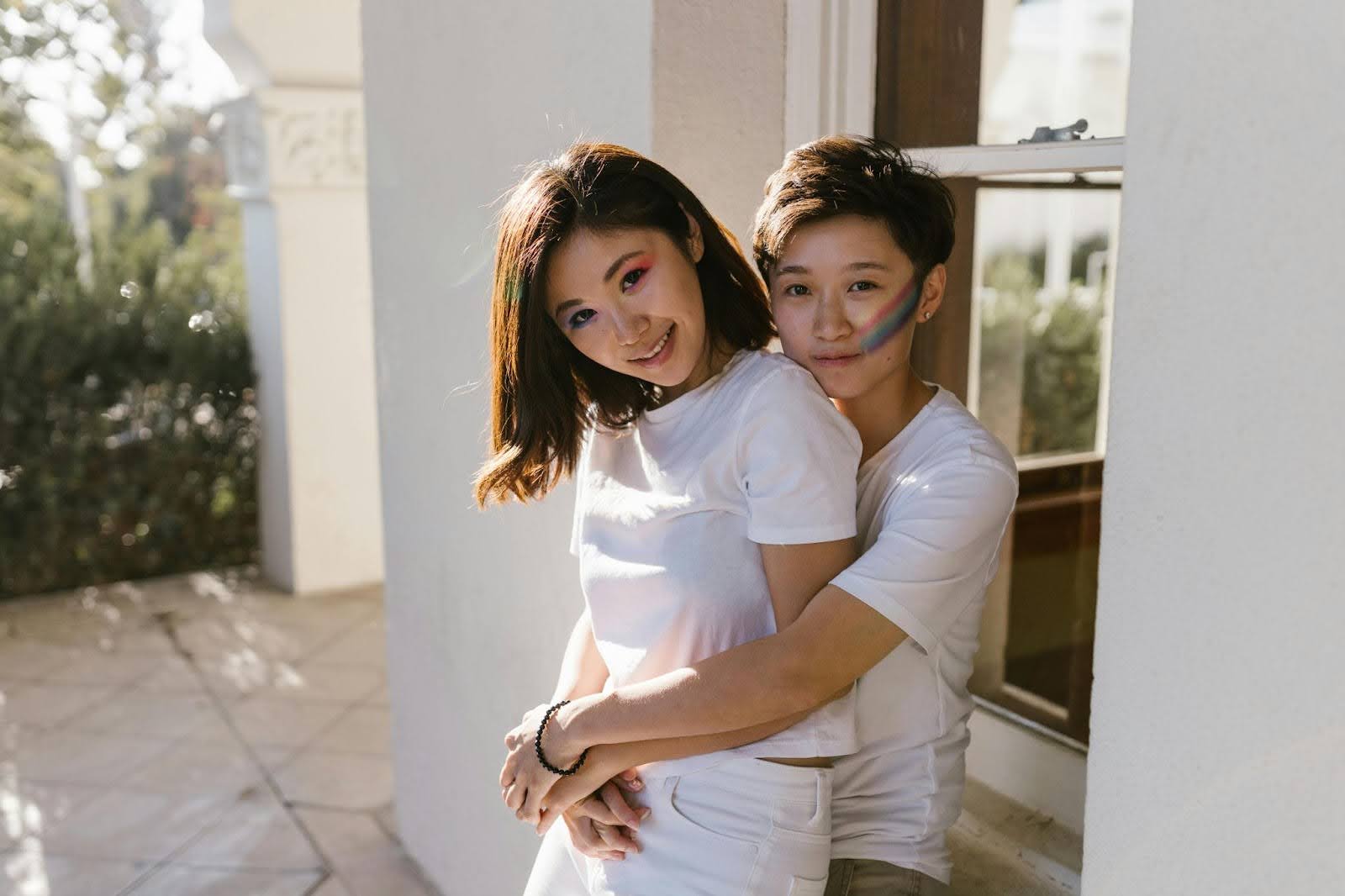 Two Asian lesbians, one hugging the other from behind