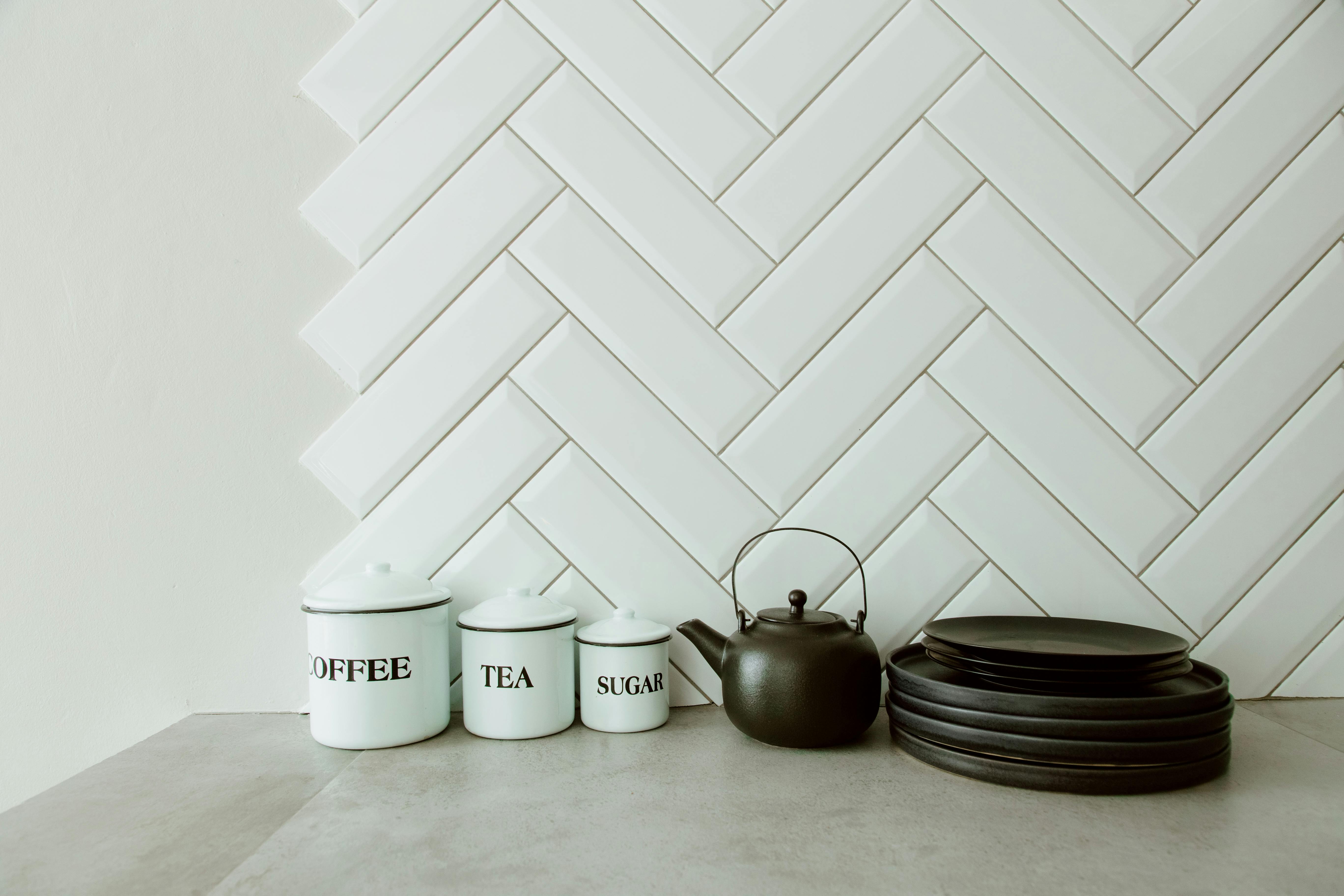 Stylish kitchen countertop setup with coffee, tea, and sugar containers next to a black kettle and stacked plates.