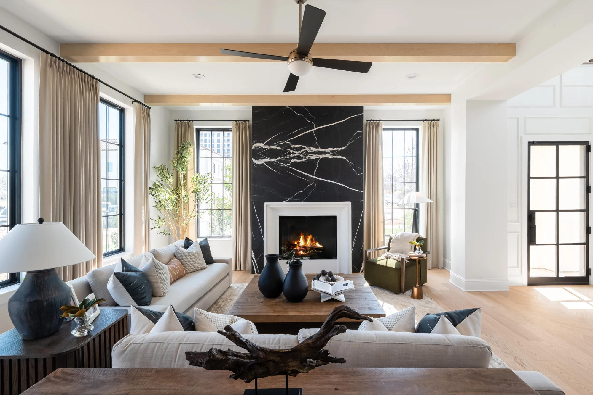 Living room with a dark stone fireplace, wood ceiling beams, and large windows at The Villas at Lakeside