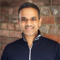 headshot photo of speaker in navy blue top against brick background