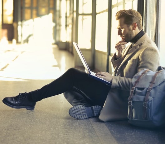 A man sitting on a floor in a railway station with laptop.