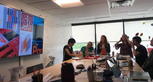 A group of designers is in JSTOR's design studio around our standing desk. We are presenting some conceptual designs on our large tv screen on the wall.