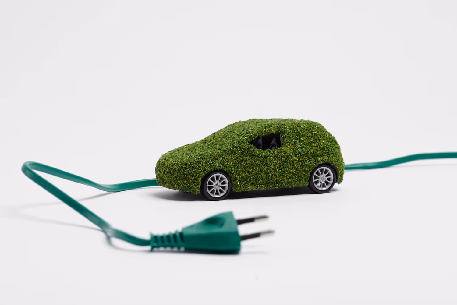 Miniature car covered in green foliage connected to a green electric plug symbolizing an ecological electric vehicle.
