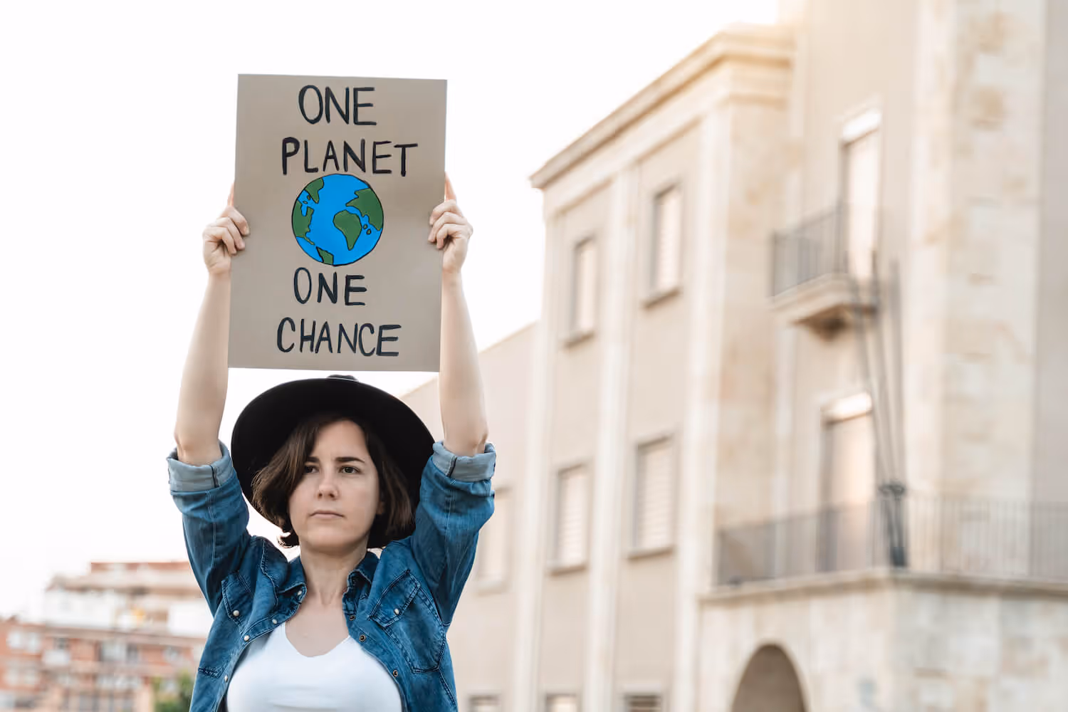 Woman wearing a black hat and denim jacket holding a sign that reads 'ONE PLANET ONE CHANCE' with an illustration of Earth.