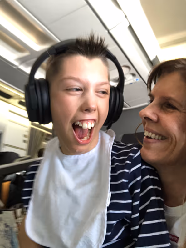 Smilende gutt med hodetelefoner sitter på fanget til mammaen sin