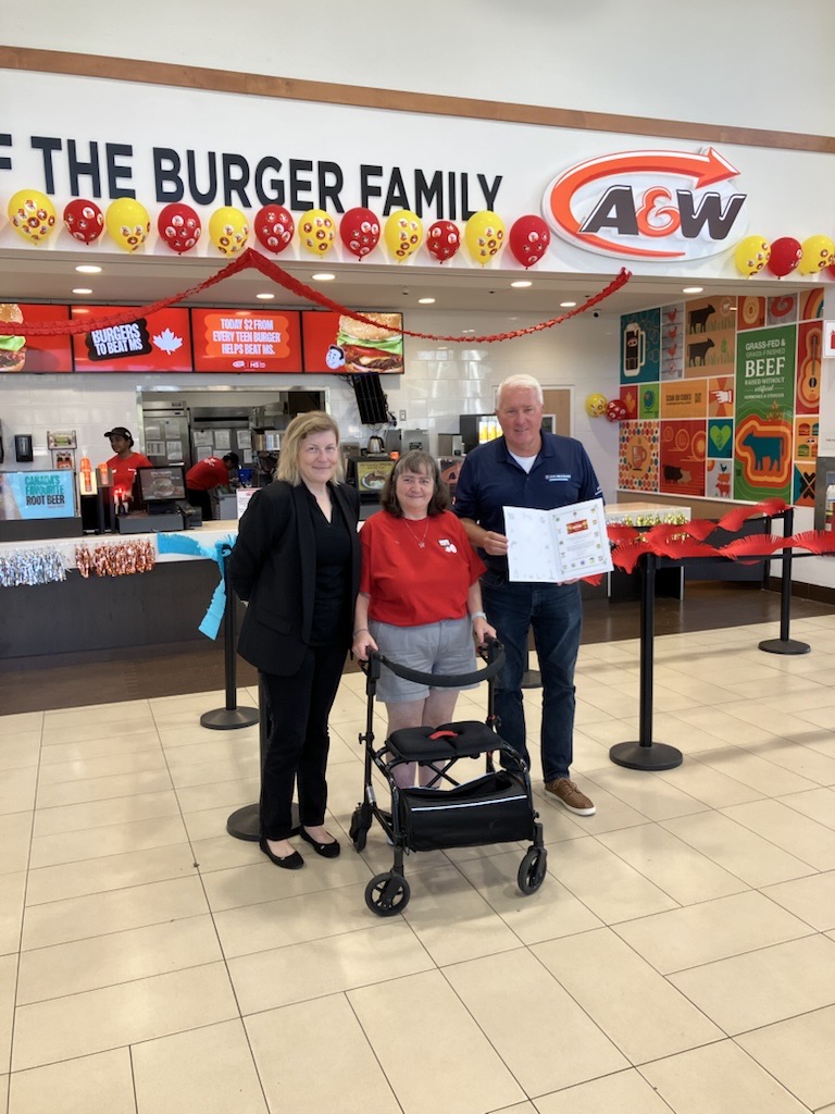 Three people in front of A&W with decorations for Burger to Beat MS