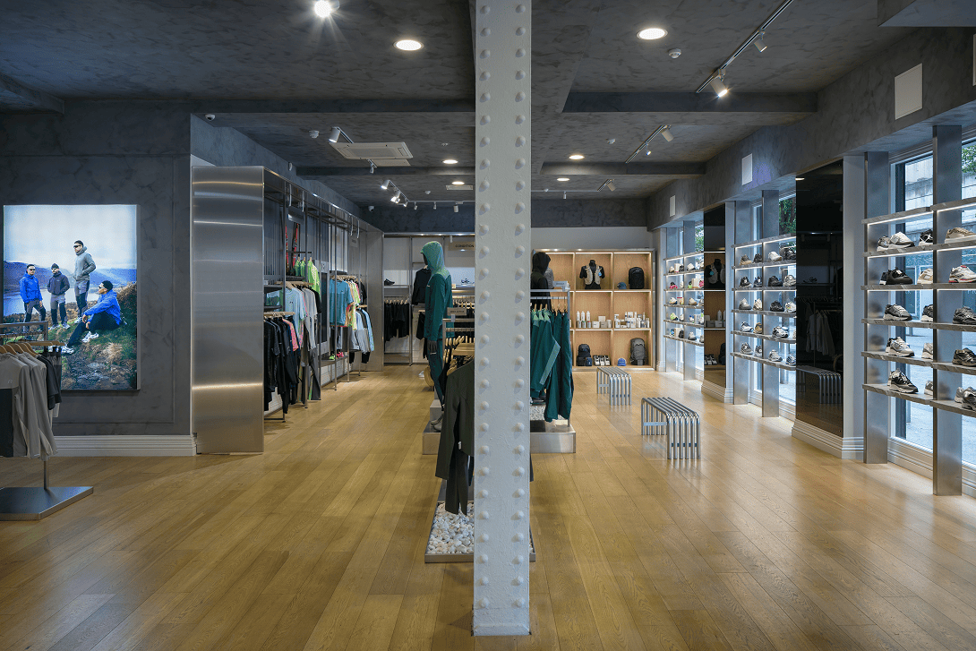 Main sales floor of the Drip Moda Liverpool retail store featuring modular stainless steel hanging rail display systems, handcrafted concrete shelving with integrated recessed LED lighting, stainless steel support columns and limewash decorative finishes installed by Bobblehat.