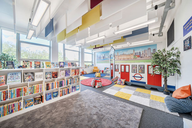 Bright and colorful children's reading room with bookshelves, a London-themed play area, cushions, and large windows.